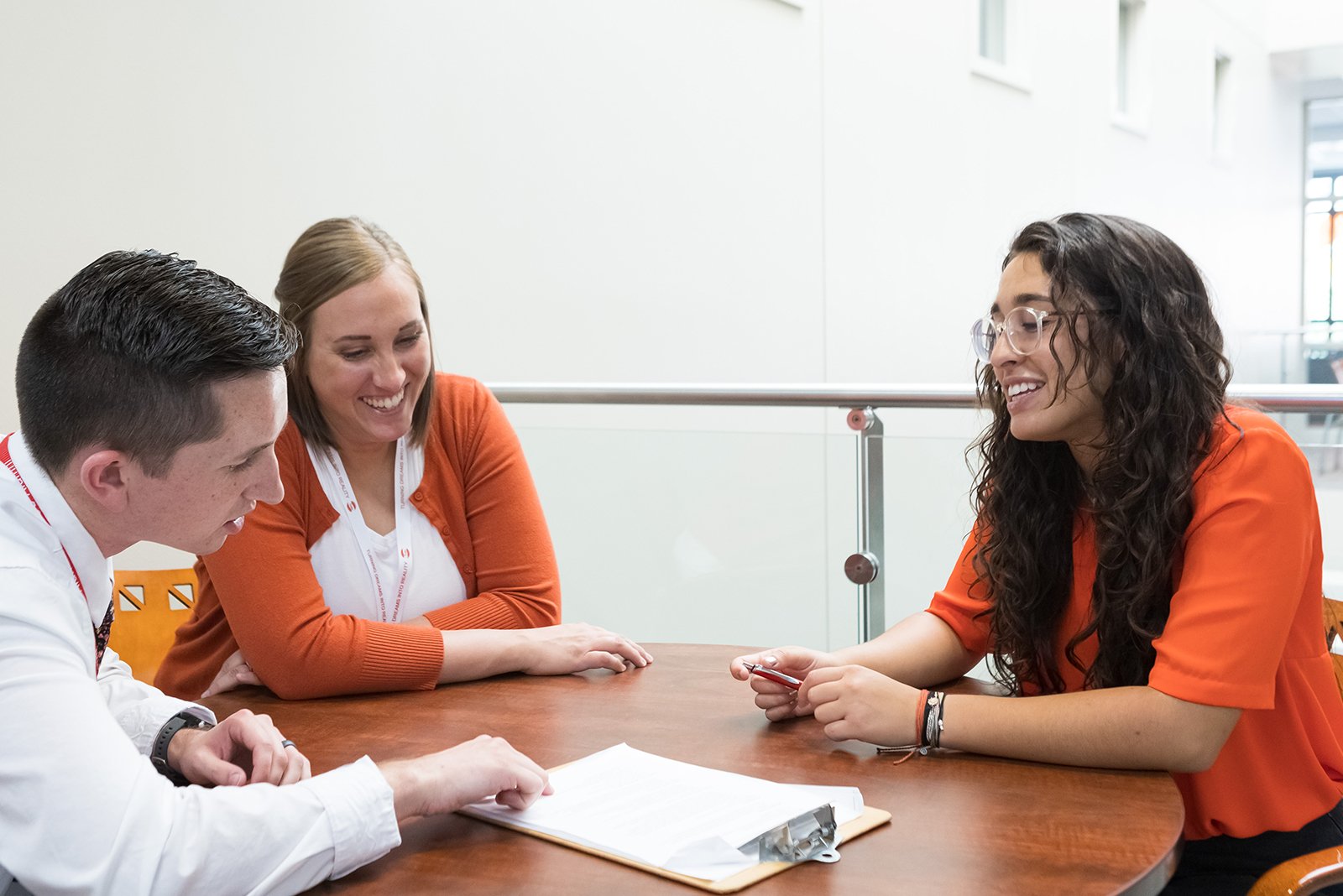 business students sitting at a table discussing notes on a clipboard