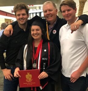 Southern Utah University RN to BSN graduate Ashlee Cornell smiling in cap and gown at graduation holding diploma and standing with her husband and two adult sons